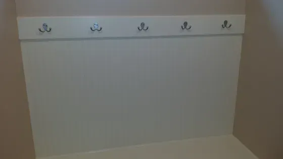 White wall with five silver hooks above a built-in white bench.