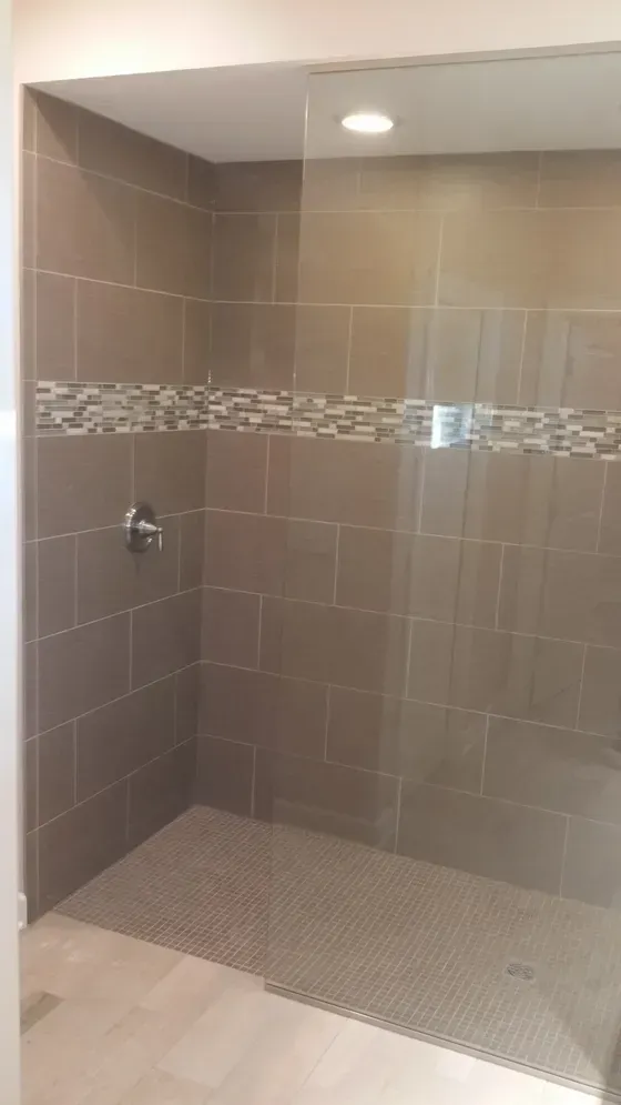 Bathroom shower with brown tile walls, a decorative border, and glass door.