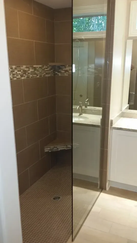 A tiled shower with a glass door, built-in bench, and accent tile. The bathroom features a sink and window.