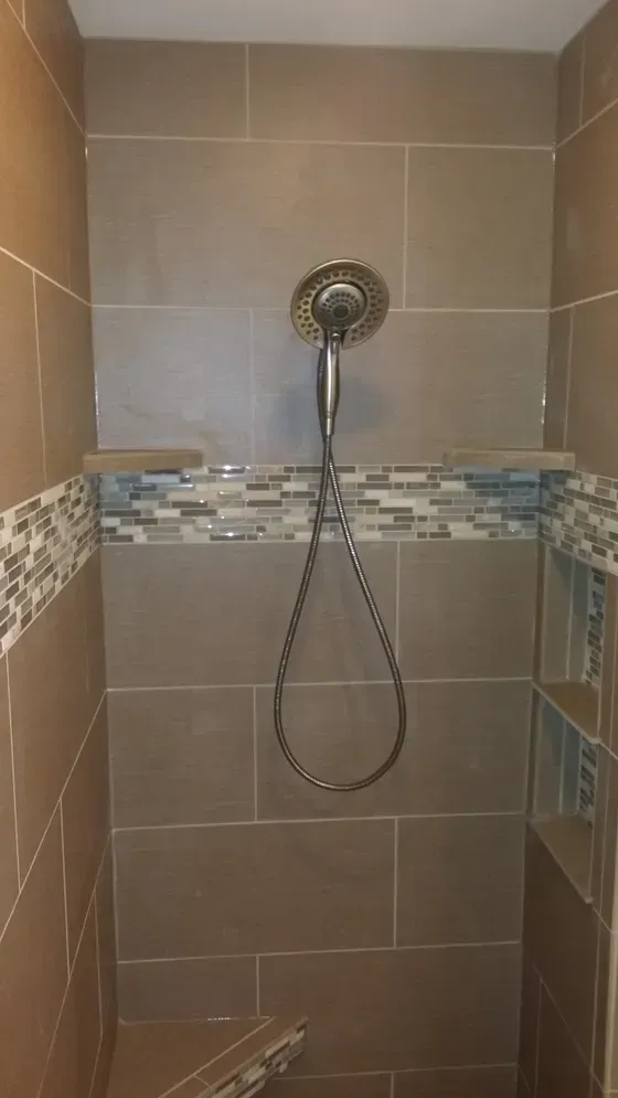 Tiled shower with a showerhead, accented with mosaic tile. Brown and blue tones.