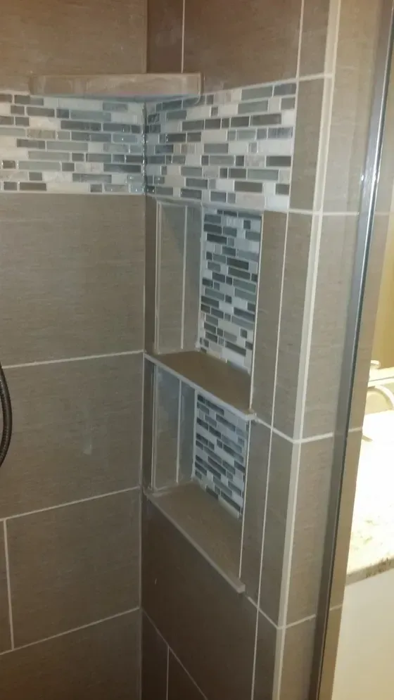 Shower with built-in shelves. Beige tiles with accent mosaic.