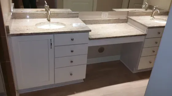 White bathroom vanity with two sinks, granite countertops, and desk area.
