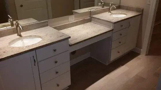 Bathroom vanity with two sinks and a seated vanity area. Light granite countertops. White cabinets, silver fixtures.