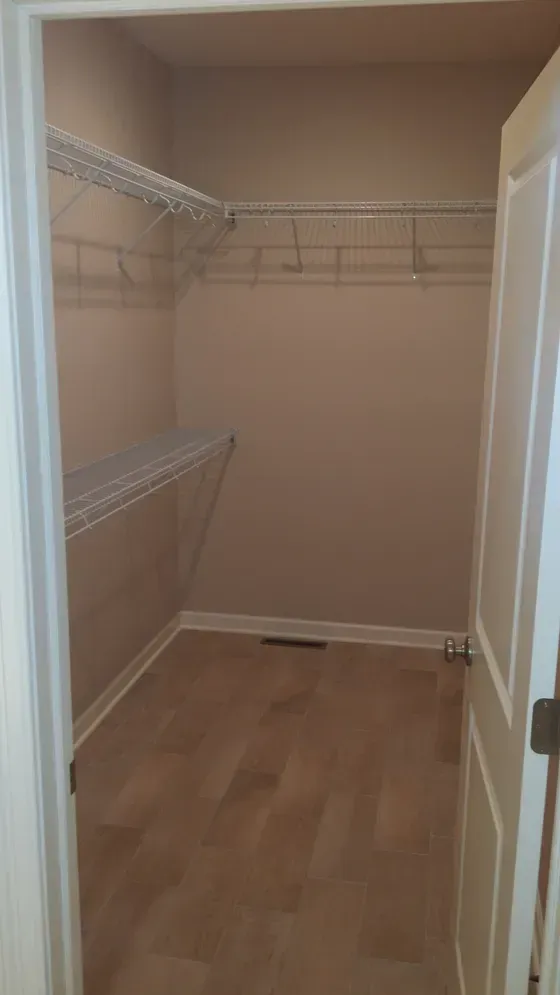 Empty closet with wire shelves, tan walls, and wood floor.