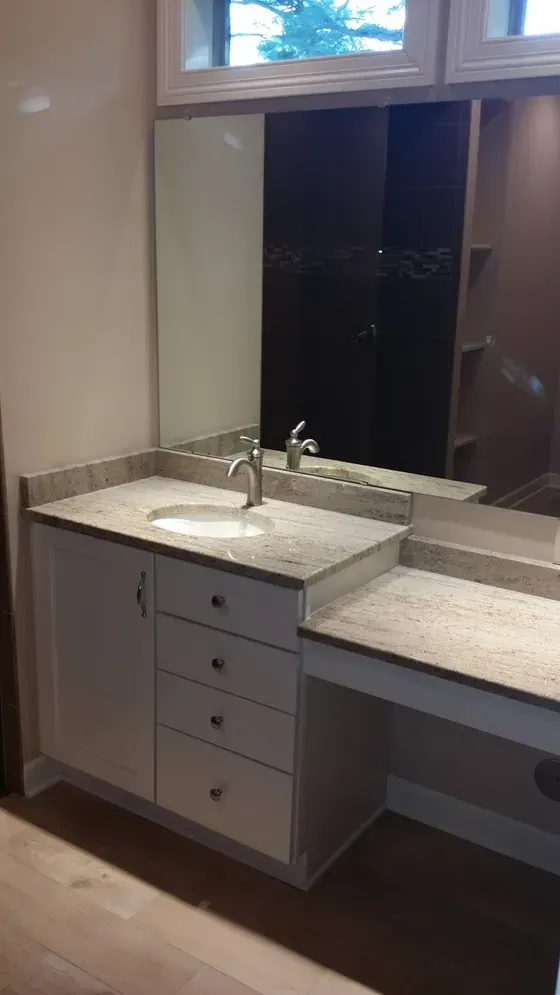 Bathroom vanity with white cabinets, granite countertop, sink, mirror, and vanity area.