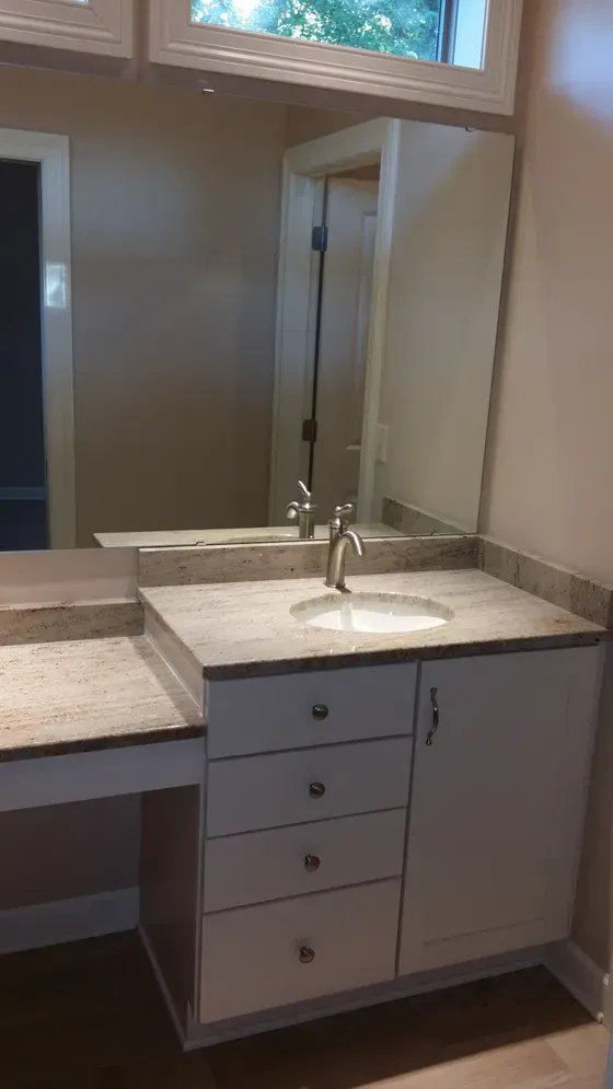 Bathroom vanity with white cabinets, granite countertop, mirror, and sink.