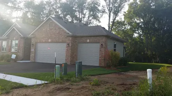 Two-car garage of a brick house with gray doors, set in a grassy yard, with trees in the background.