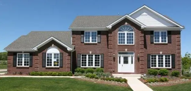 Brick two-story house with white trim, a white front door, and a blue sky backdrop.