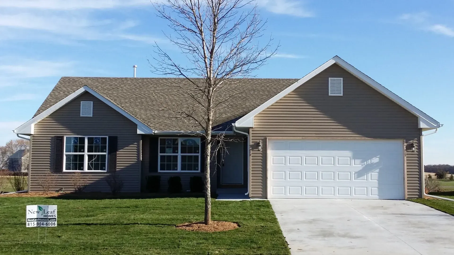 Tan and white house with a two-car garage, tree in front, set against a blue sky.