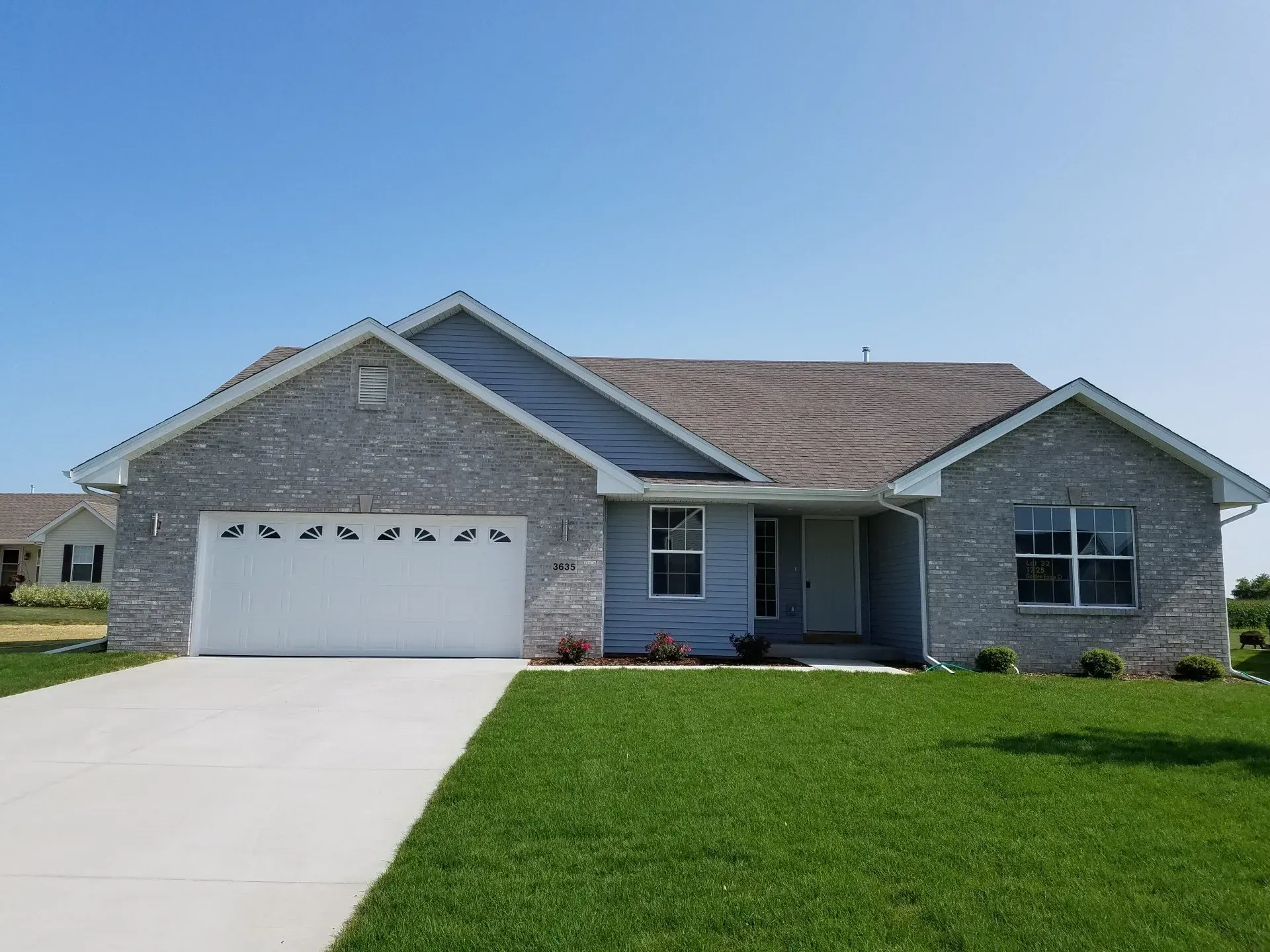 Single-story house with gray brick exterior, white garage door, and green lawn under a blue sky.