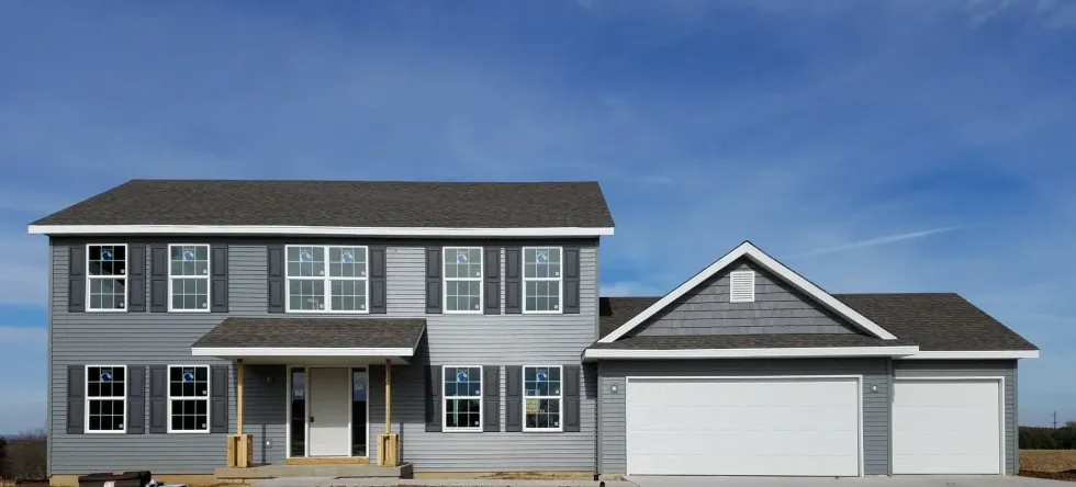 A two-story house under construction with gray siding, a dark roof, and a two-car garage.