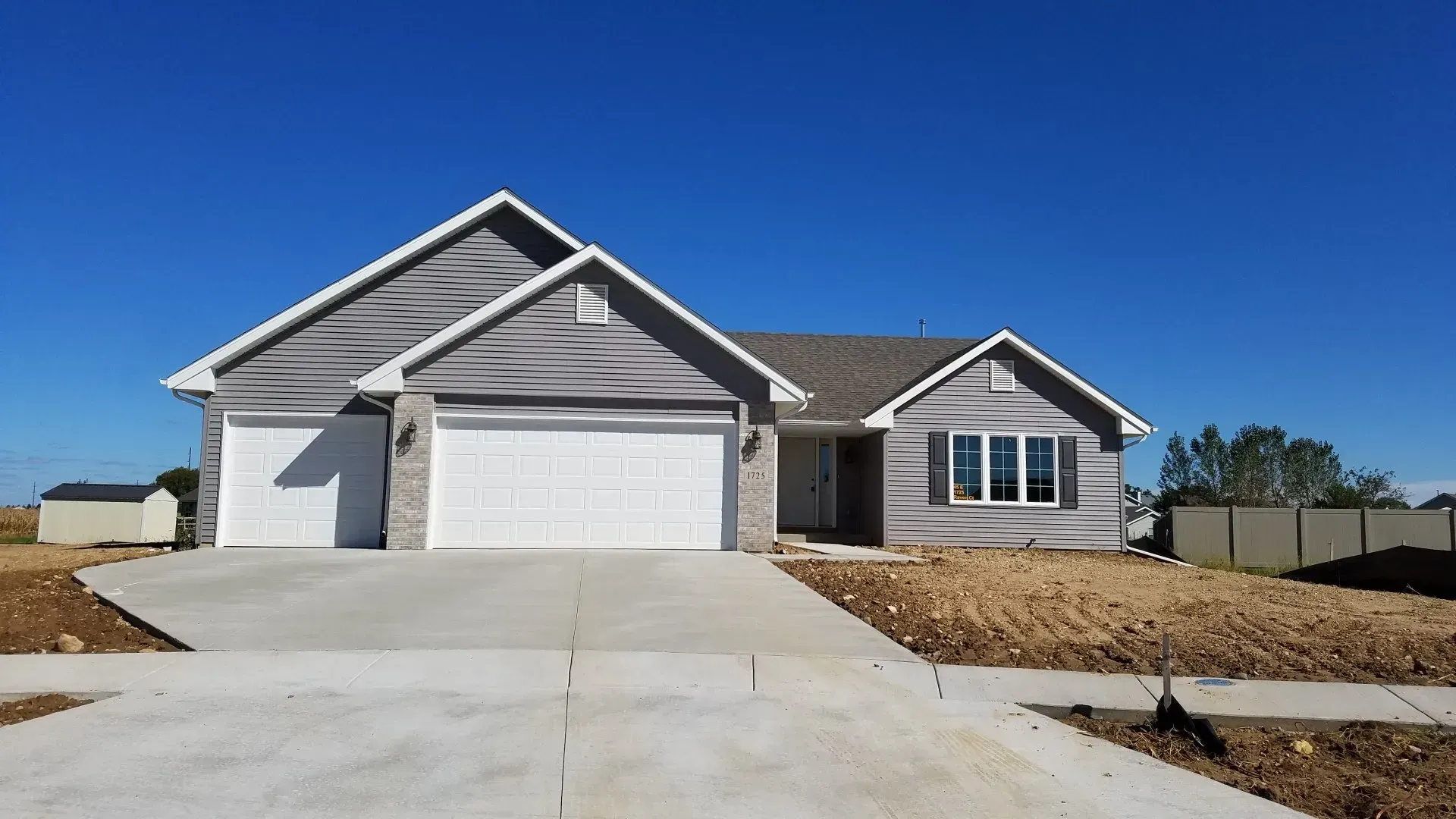 New gray house with white garage doors, concrete driveway, and a blue sky.