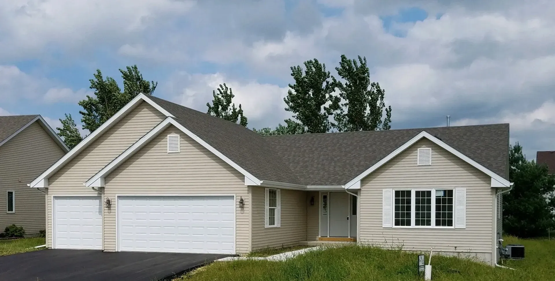 Beige house with white garage doors and trim under a cloudy sky.