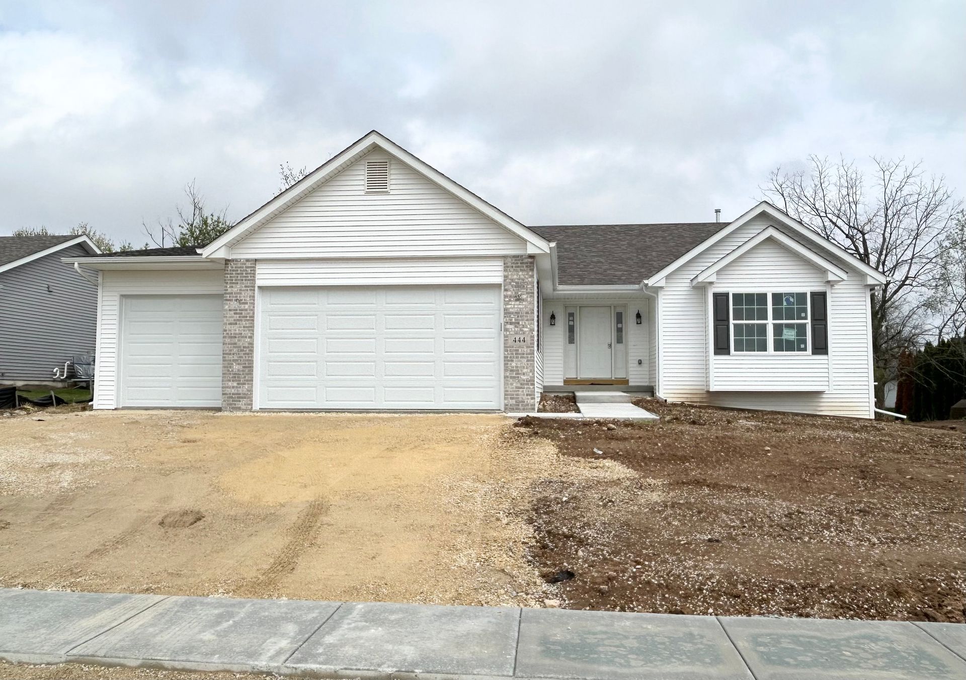 White house with two-car garage and bay window. Gravel yard, unfinished landscaping.