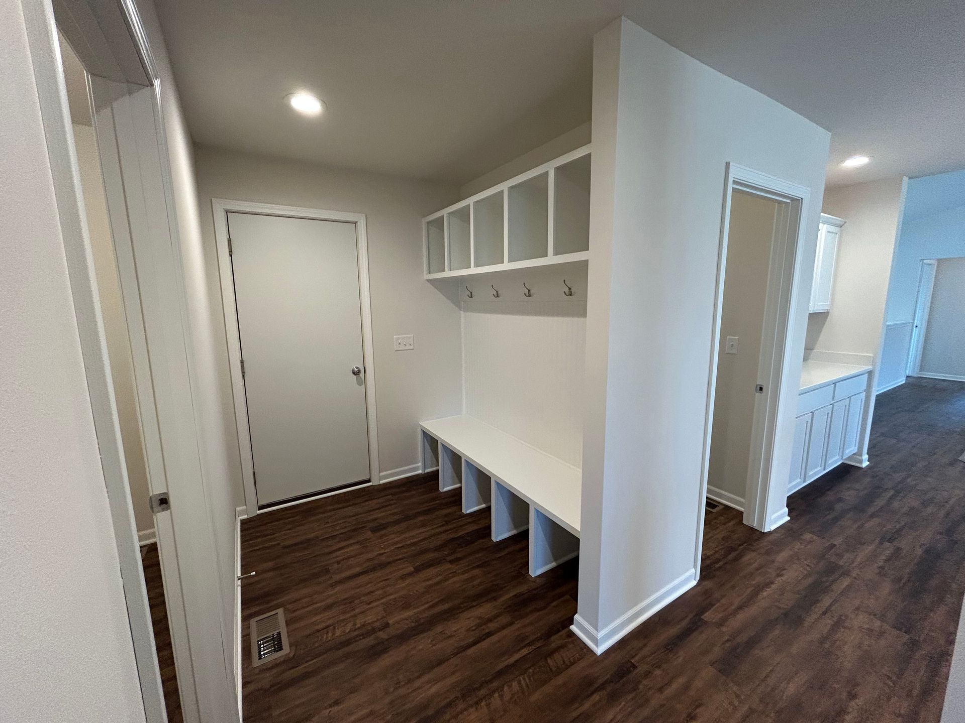 Mudroom with built-in white bench, cubbies, and coat hooks on wood flooring. A door is visible in the background.