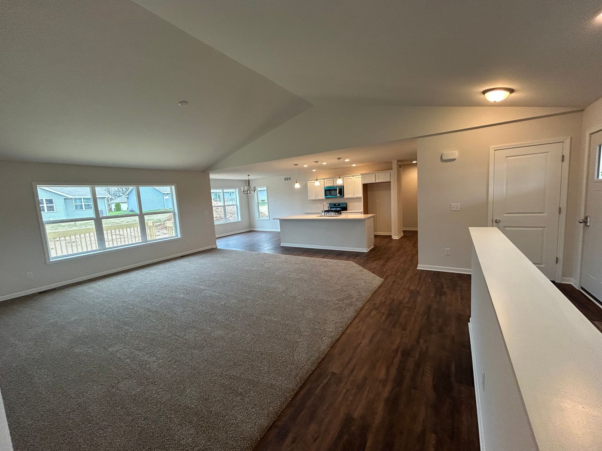 Open-concept living space with carpeted living area, wood floors, and kitchen with island.