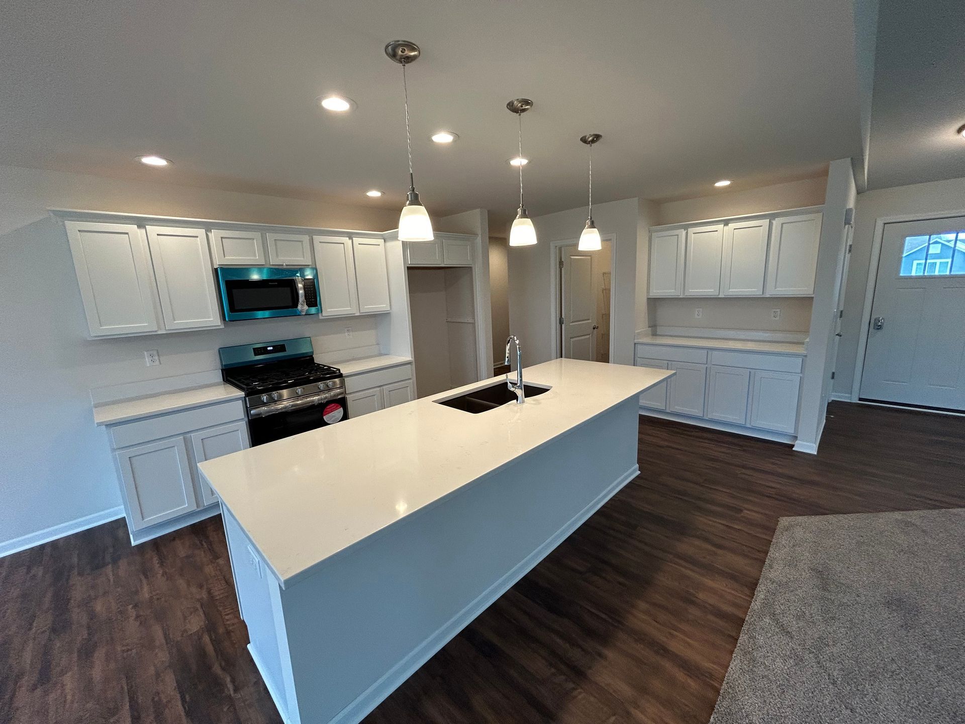 Spacious white kitchen with an island and a gas stove, with dark wood floors and a gray carpet.