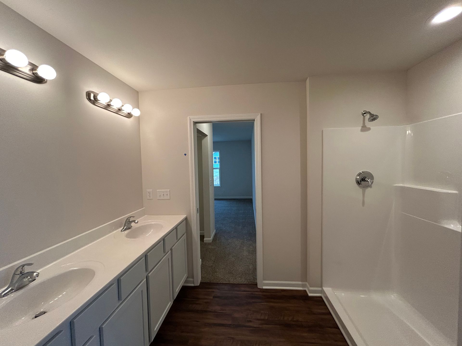 Bathroom with double sink vanity, shower, and door to bedroom; neutral colors.