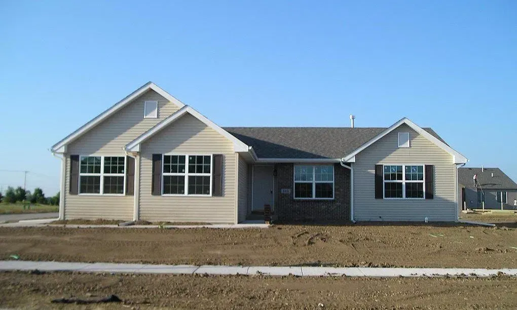 Tan ranch house with gray roof and black shutters, set on a new construction lot.