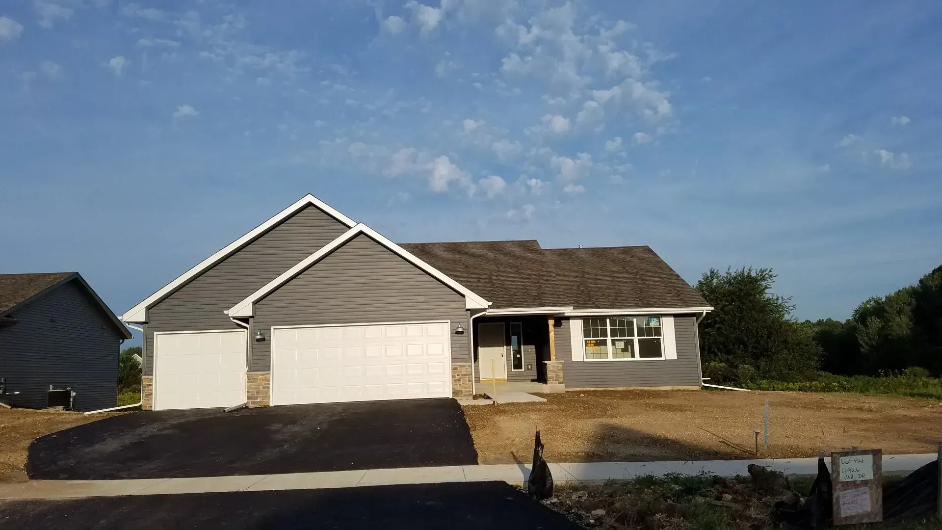 New house with gray siding, white garage doors, and brown roof under a blue sky.