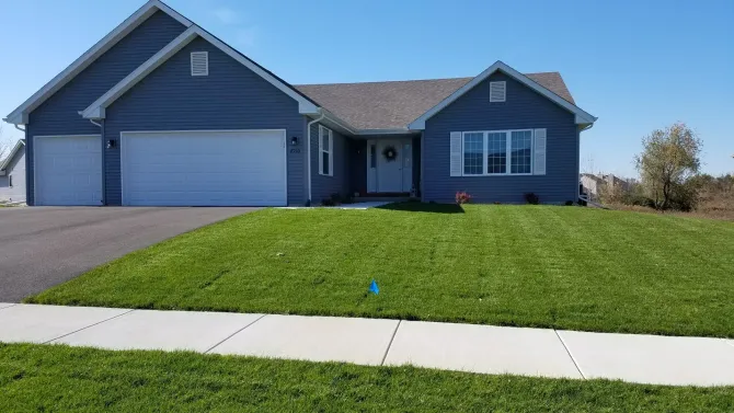 Blue house with white trim, green lawn, and a paved driveway on a sunny day.