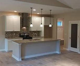 A modern kitchen with white cabinets, a gray island, and pendant lights. A decorative backsplash and a stainless steel range hood are also visible.