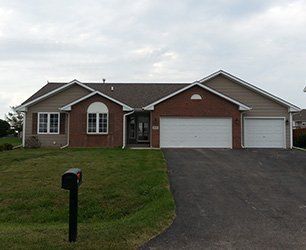 Ranch-style house with brick and tan siding, two-car garage, driveway, and lawn. Black mailbox in foreground.