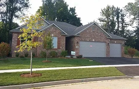 Brick house with gray garage doors, green lawn, and trees under a blue sky.