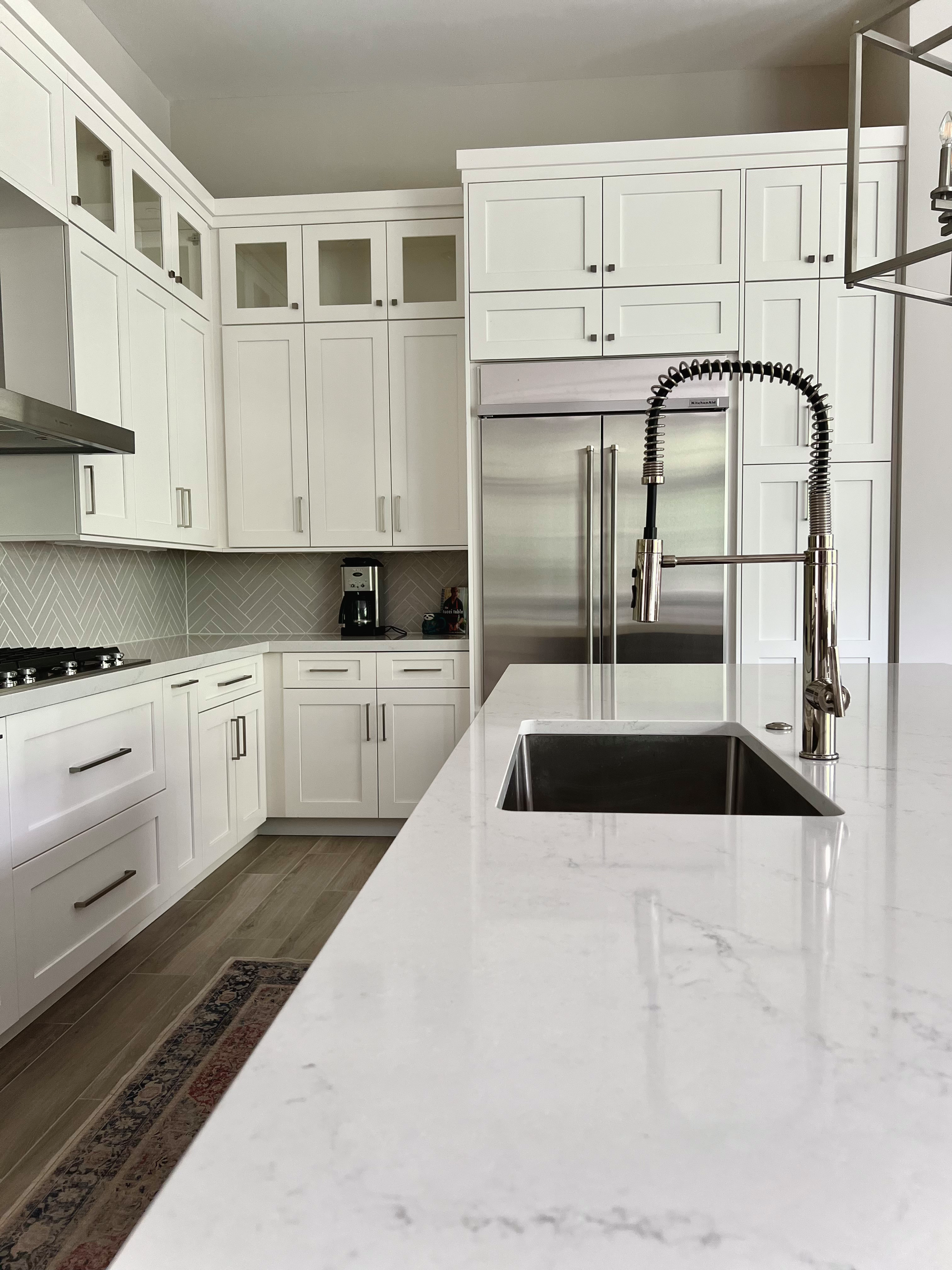 White kitchen with marble countertops, stainless steel appliances, and a large sink.
