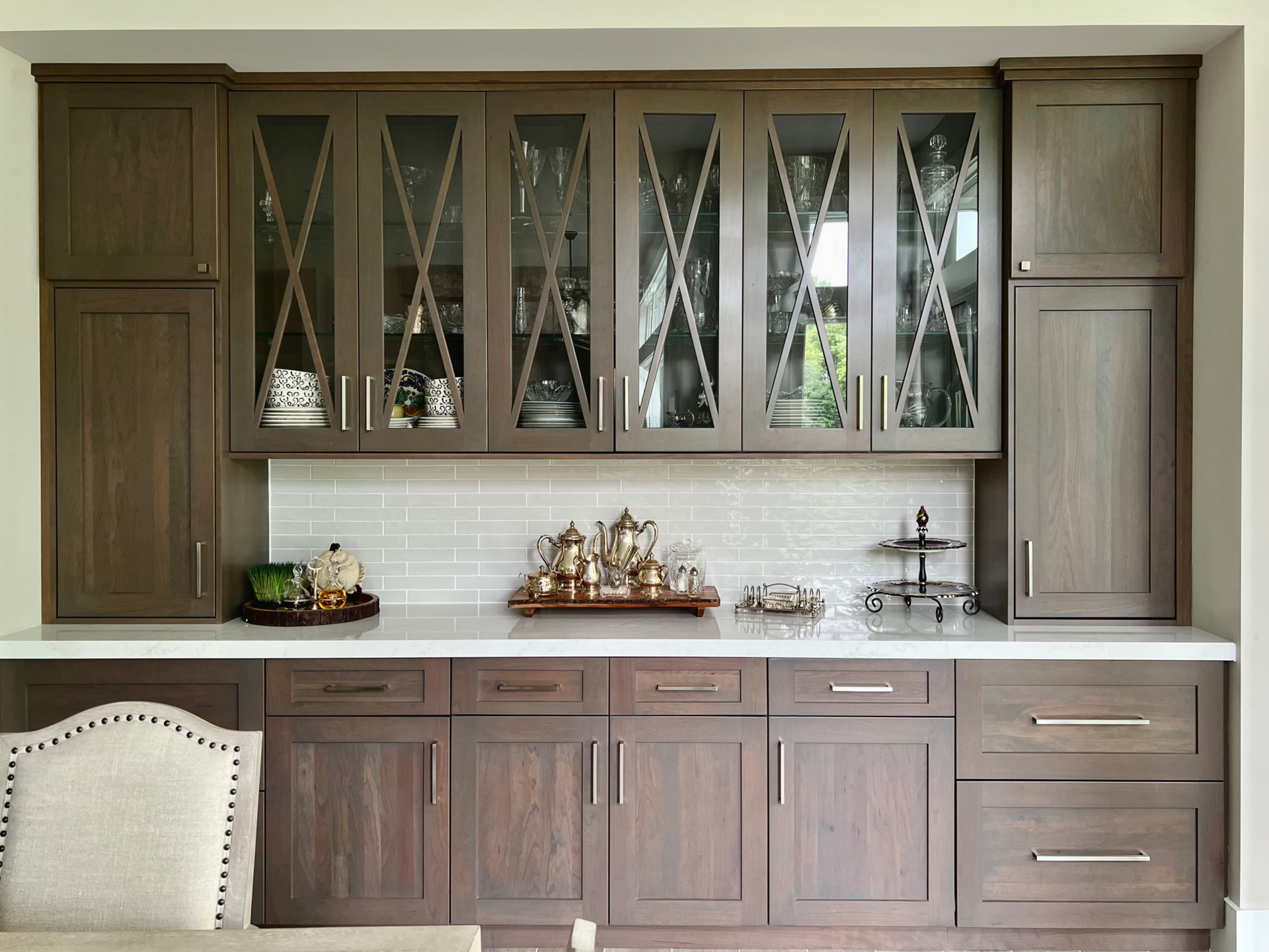 Built-in wooden kitchen cabinets with glass-front uppers, holding dishes, over a white countertop.