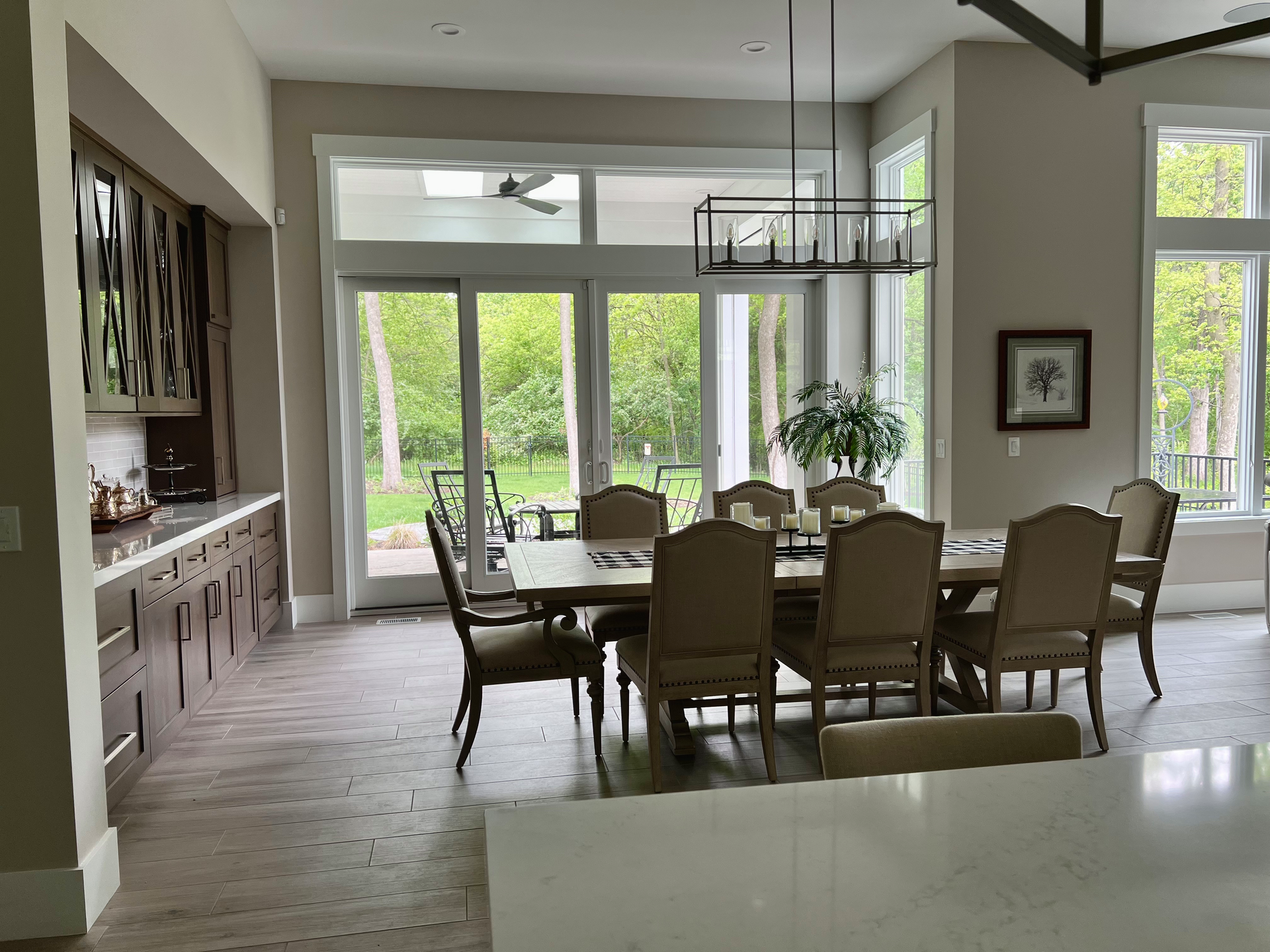 Elegant dining room with a large table, chairs, and view of greenery through large windows.