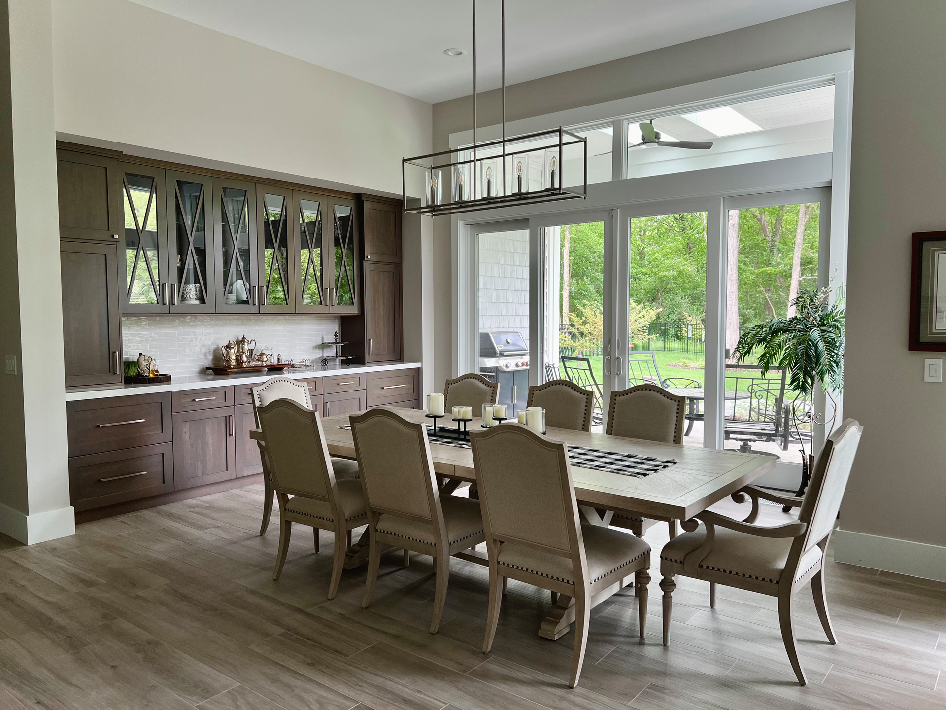 Elegant dining room with a table set for a meal, cabinets, and a large window overlooking a green landscape.