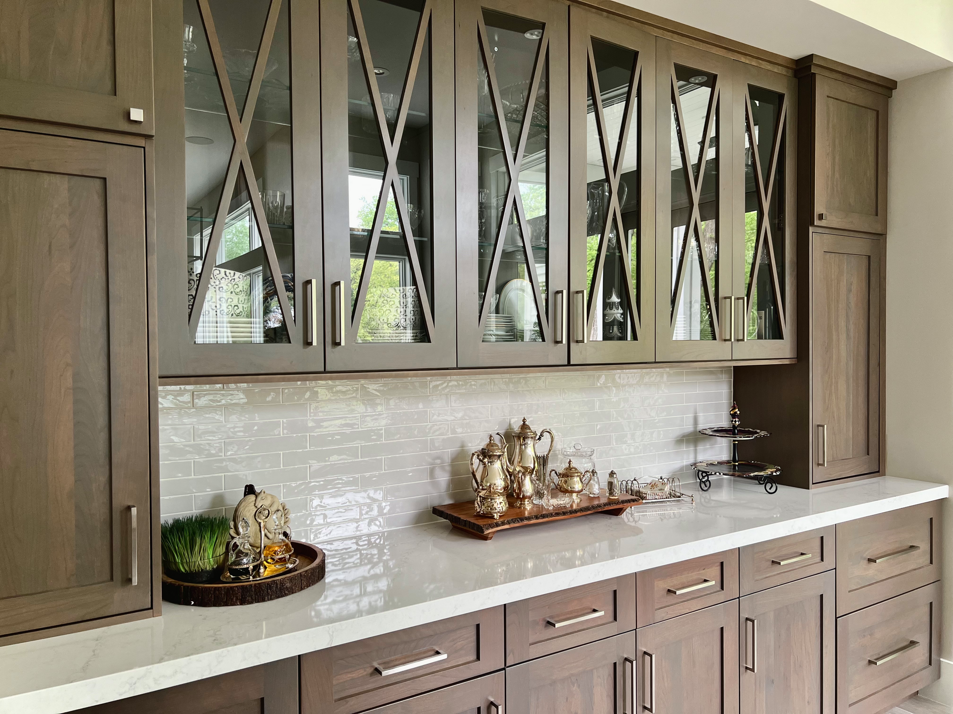 Wooden cabinetry with glass-front uppers, a white countertop, and a mosaic backsplash; items on the counter.