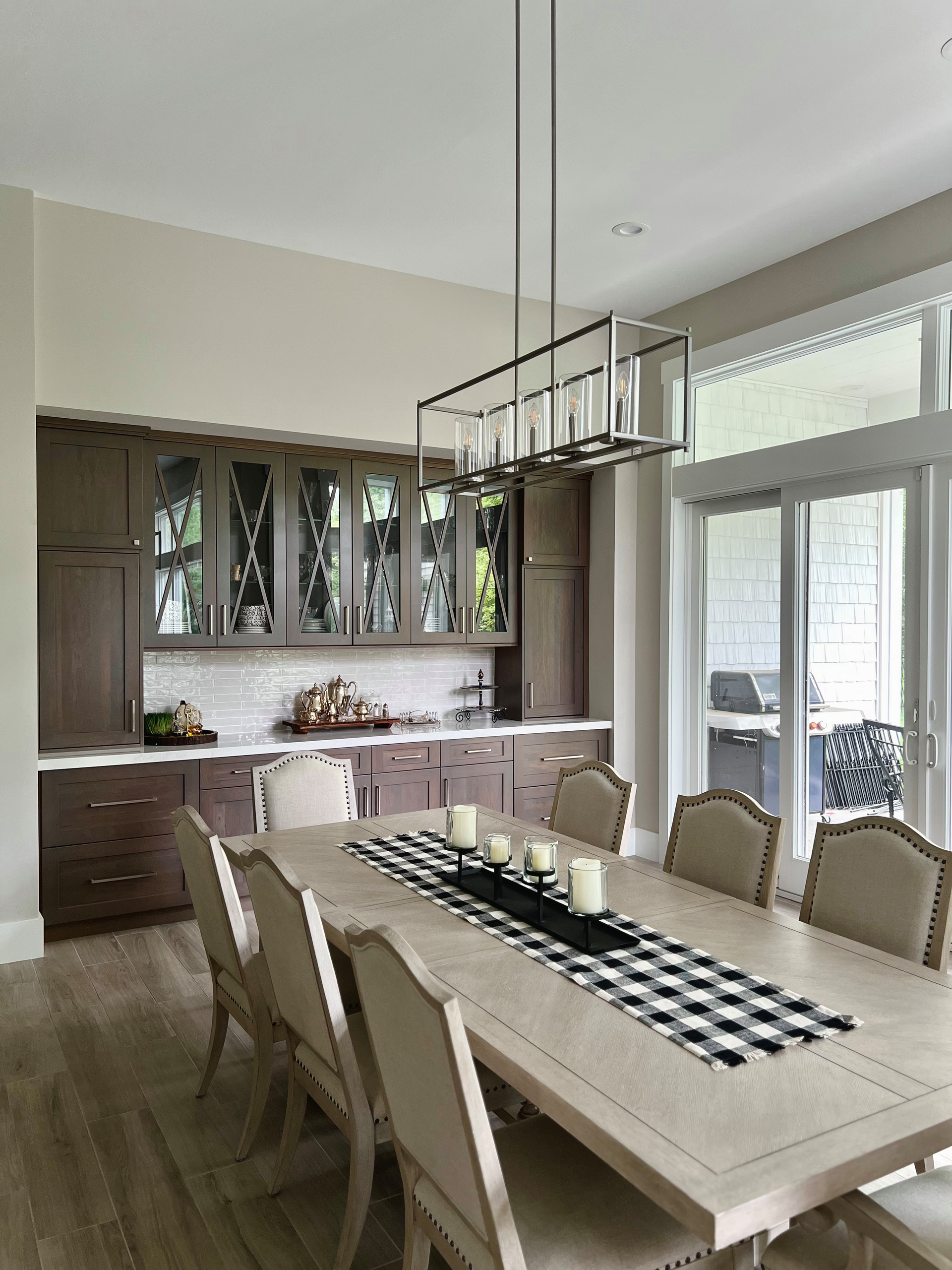 Dining room with long table, upholstered chairs, and a buffet. Light fixture hangs above.