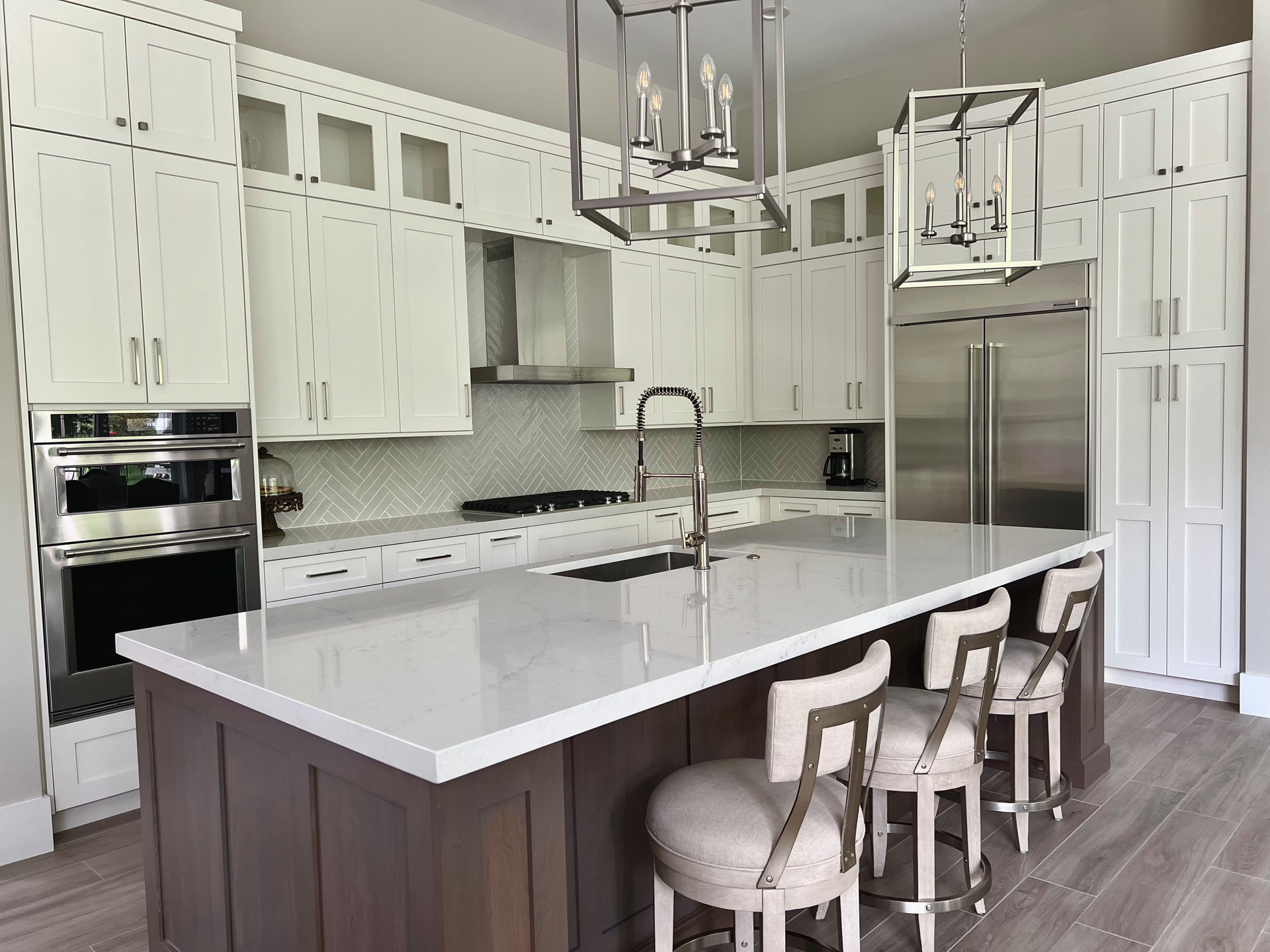 Modern white kitchen with island, stainless steel appliances, and light-colored wood floors.