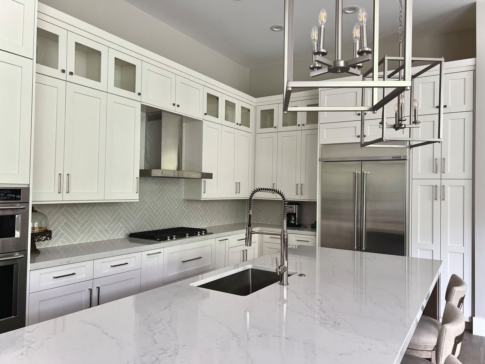 White kitchen with large island, stainless steel appliances, and modern chandelier.