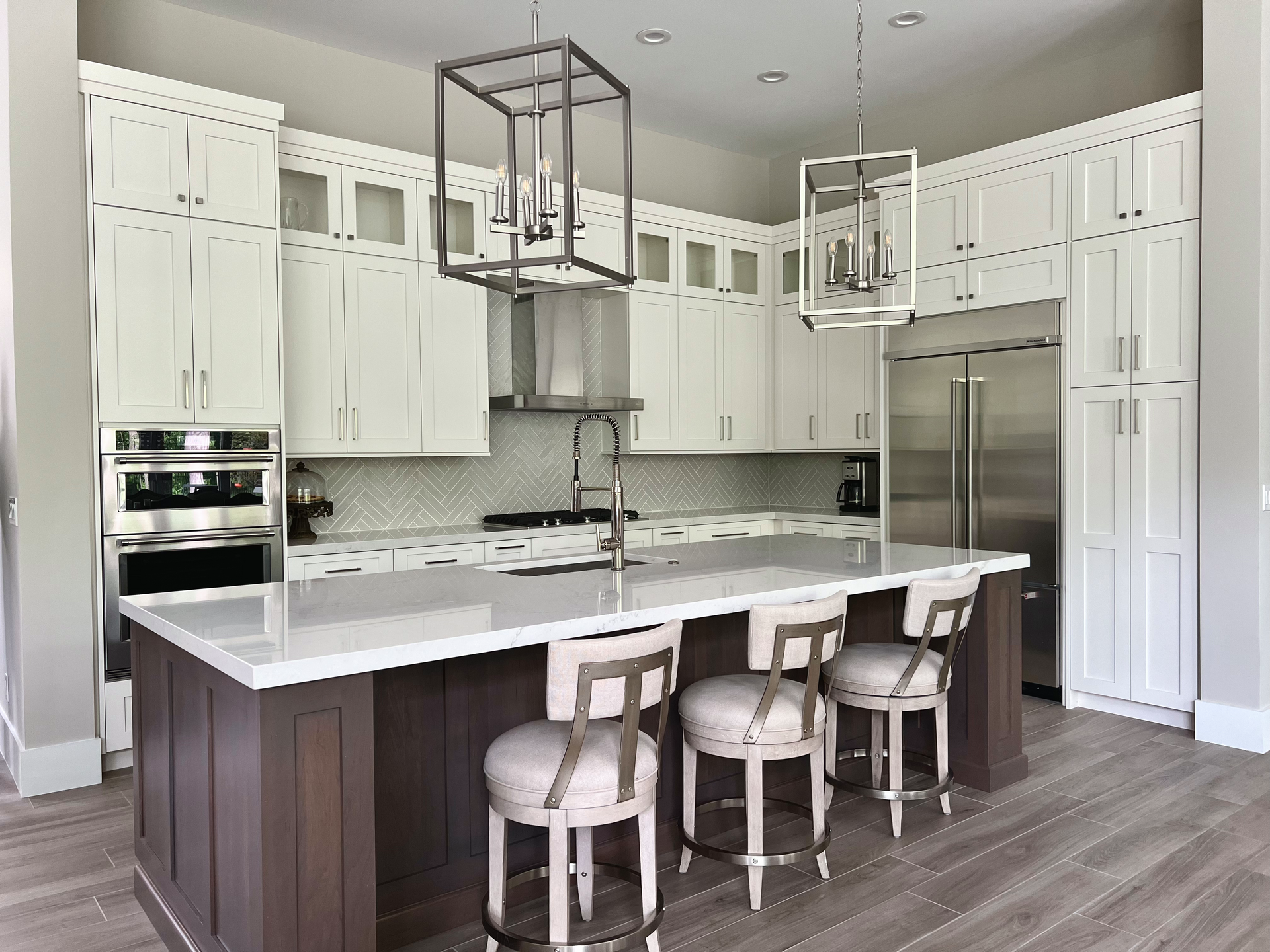 Spacious white kitchen with island and stools, stainless steel appliances, and two pendant lights.
