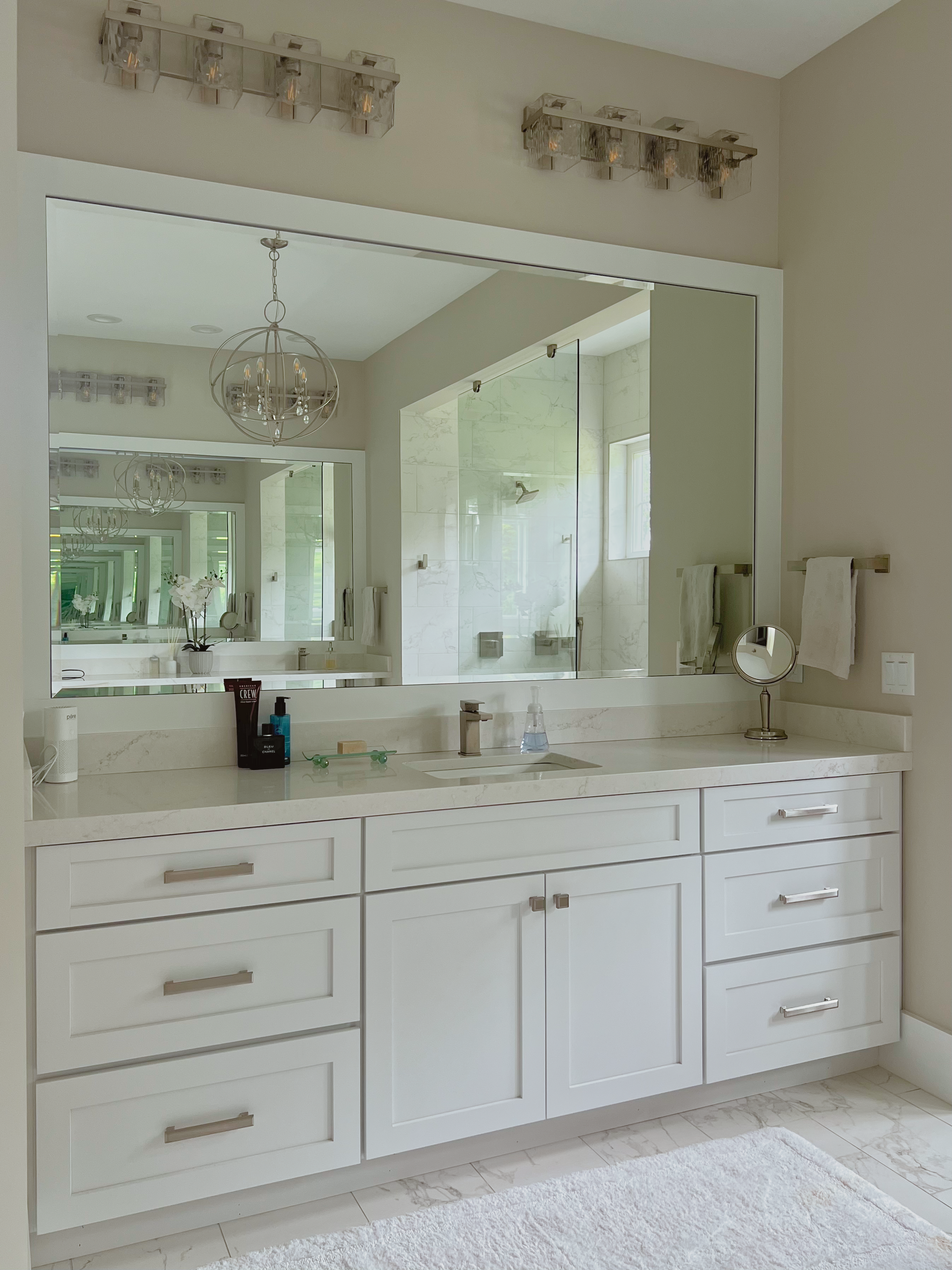 White bathroom vanity with a large mirror, lit by sconces, with sink and cabinetry.