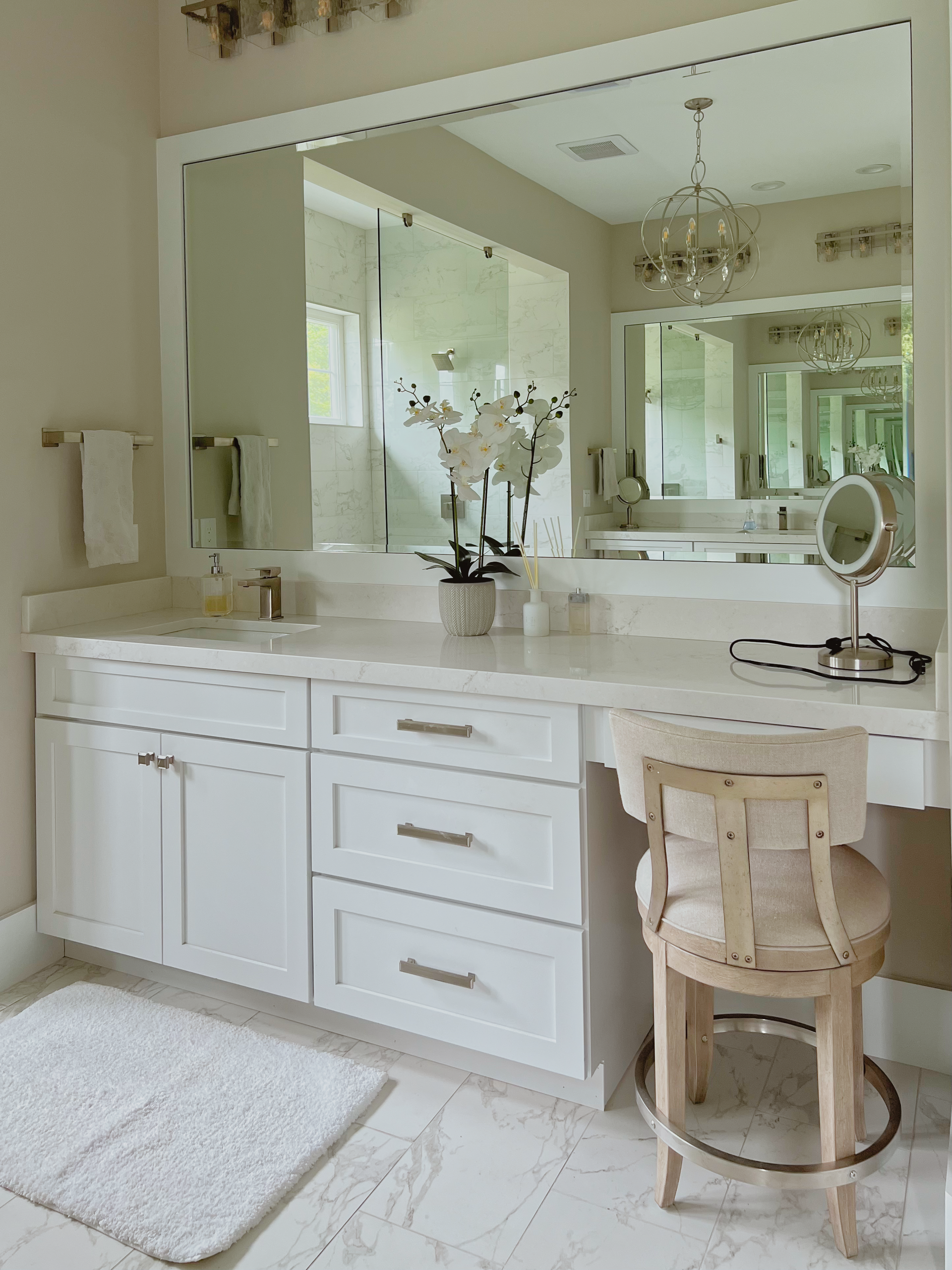 White vanity with a large mirror, drawers, and a makeup stool in a bathroom.