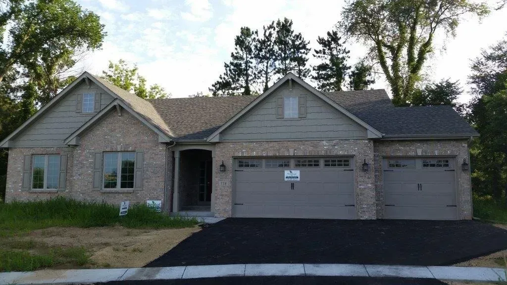 New construction house with brick facade, gray roof, and two-car garage, set in a clearing.