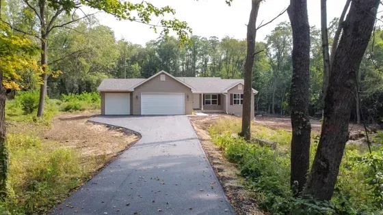Tan ranch house with asphalt driveway, two-car garage, and surrounded by trees.