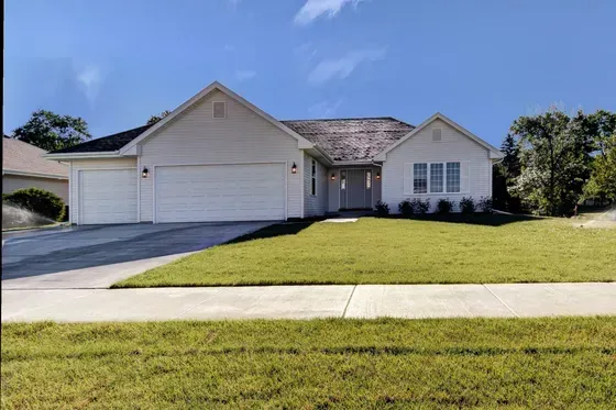 White ranch-style home with a two-car garage, green lawn, and blue sky.