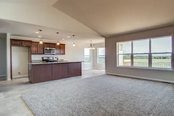 Open-concept living space with kitchen, dark cabinetry, and a large window overlooking a field.