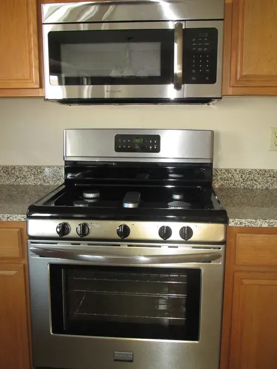 Stainless steel oven and microwave above a stovetop in a kitchen with light wood cabinets.
