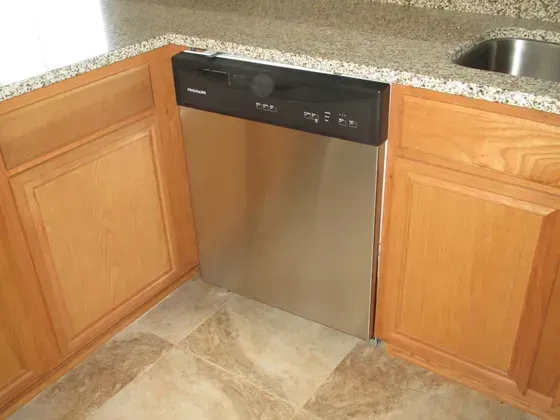 Stainless steel dishwasher in a kitchen, flanked by light wood cabinets and granite countertop.