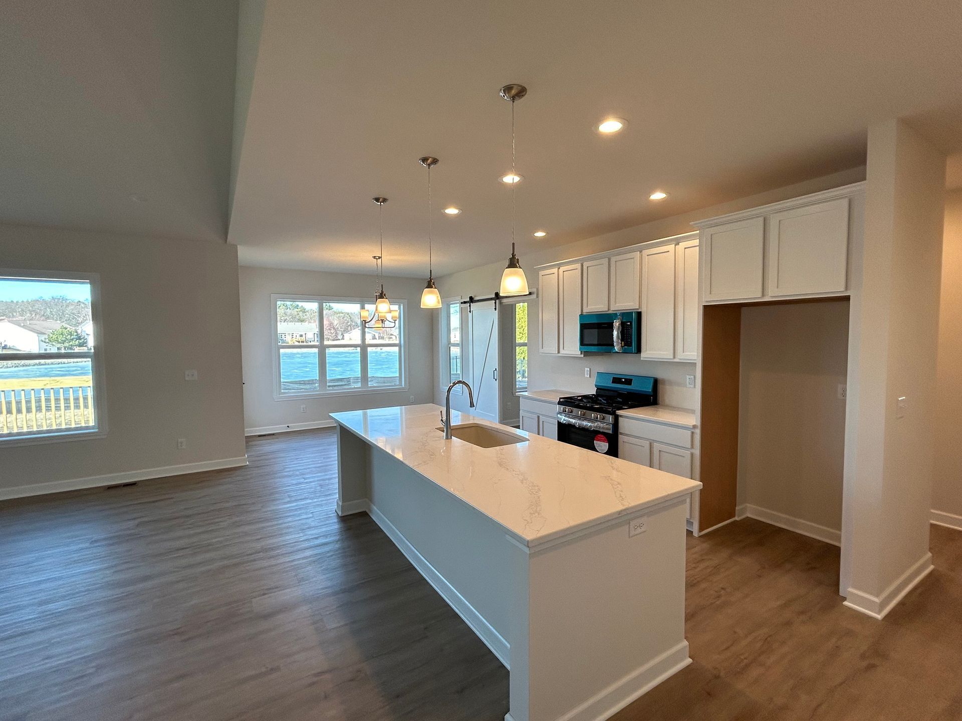 Open-concept kitchen with a white island, light blue accents, and light wood-look flooring. Windows overlook a body of water.