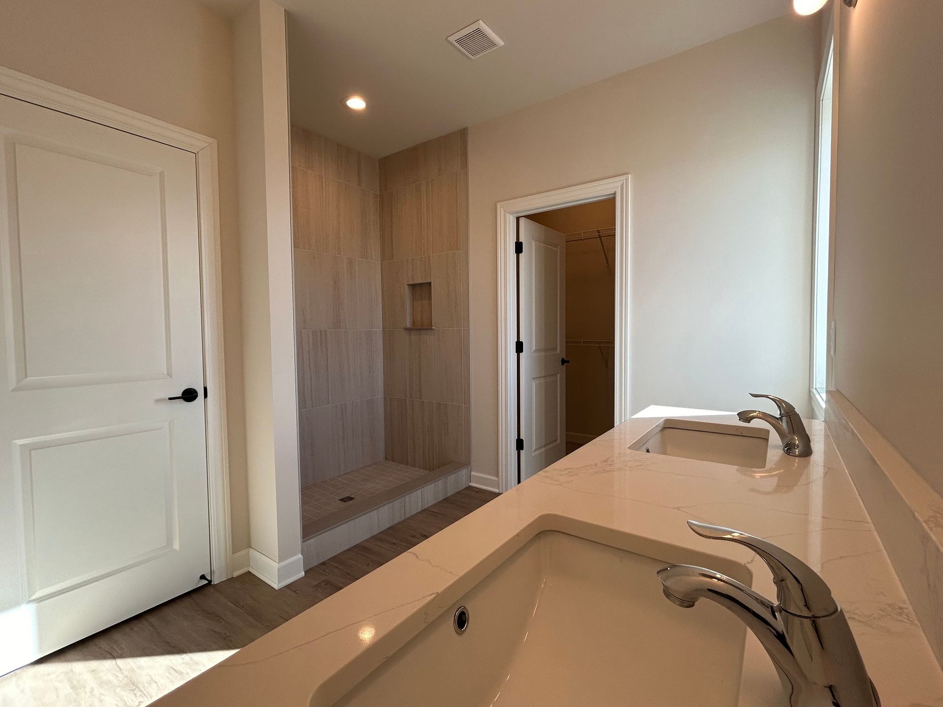 Bathroom with a double sink, a walk-in shower, and a closed door.