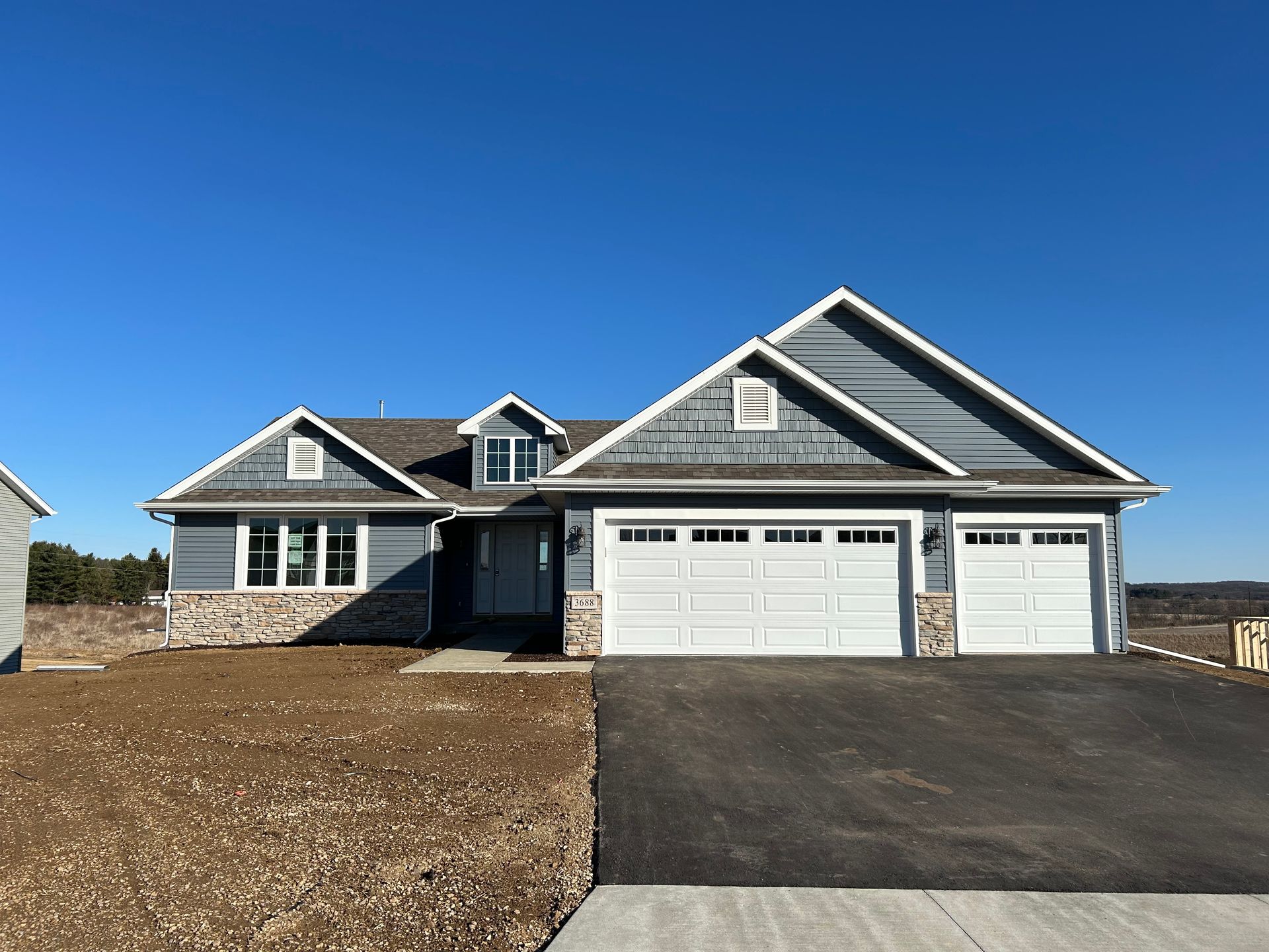 Blue-gray house with white trim, three-car garage, and stone accents under a clear, blue sky.