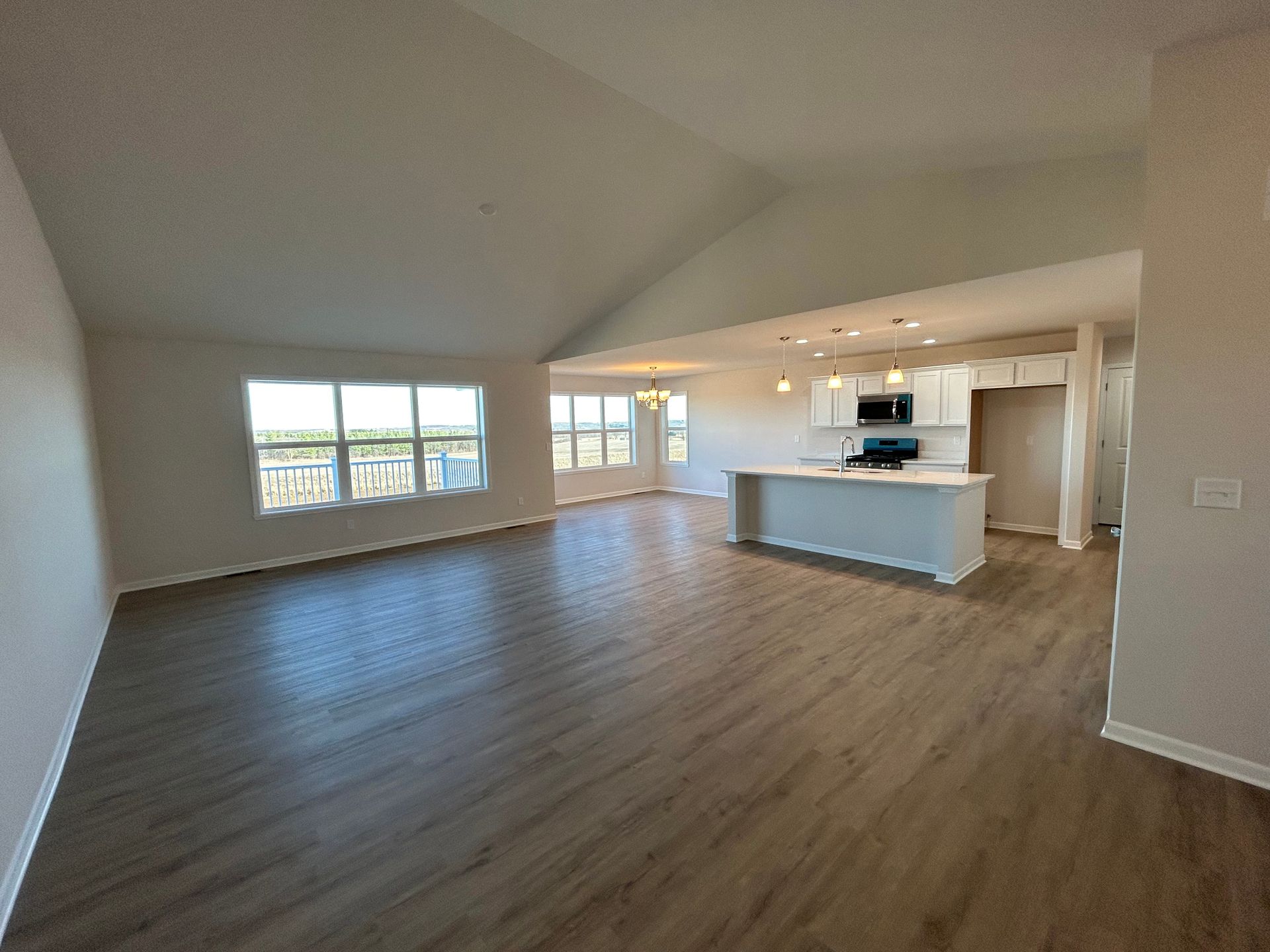 Spacious living area with wood floors, white walls, and a kitchen island. Windows and a door let in light.