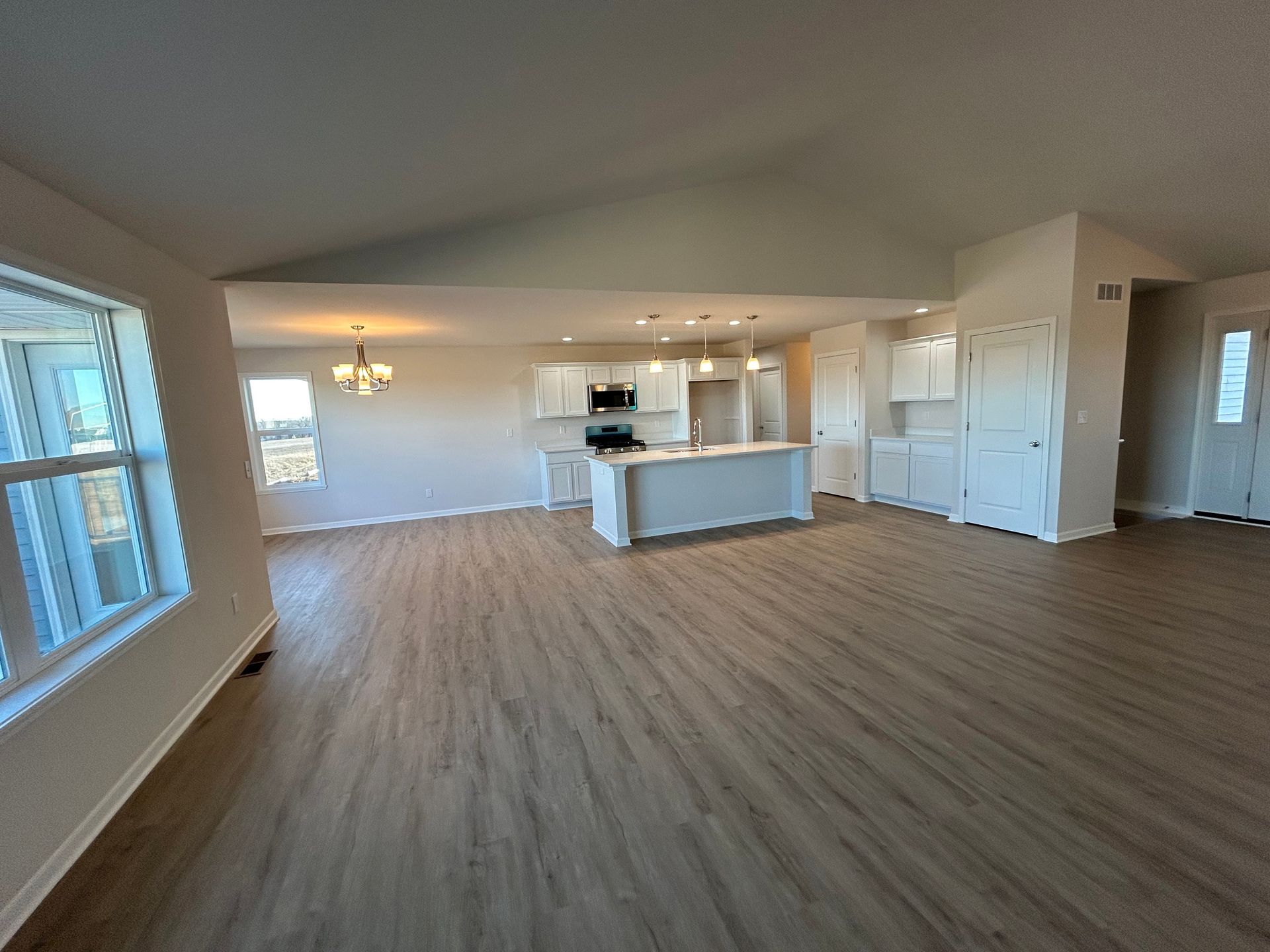 Open-concept interior with white kitchen, island, and light wood-look floors.